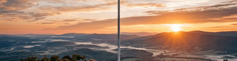 American flag on a mountain peak at sunrise with hikers walking along a rocky path